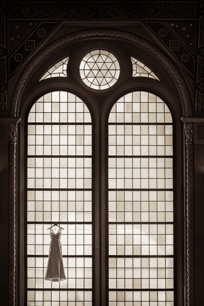 An image by Susan Stripling of a wedding dress hanging by a stained glass window won First place in the Wedding Details category of WPPI's photo competitions.